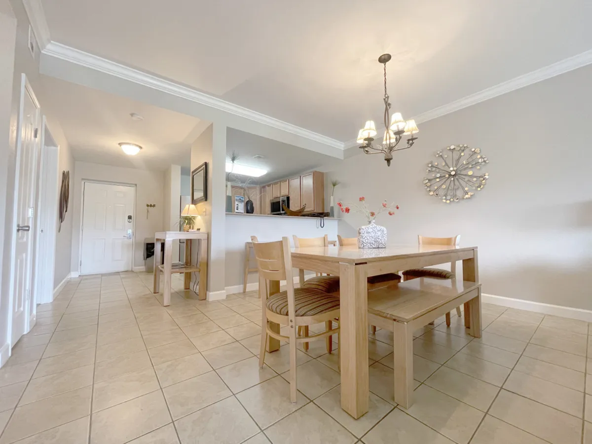 An inviting interior scene featuring a dining table under a stylish chandelier, with the entryway and kitchen visible in the background. This image showcases communal spaces where guests can relax, gather, and enjoy amenities such as cable TV and upgraded WiFi.