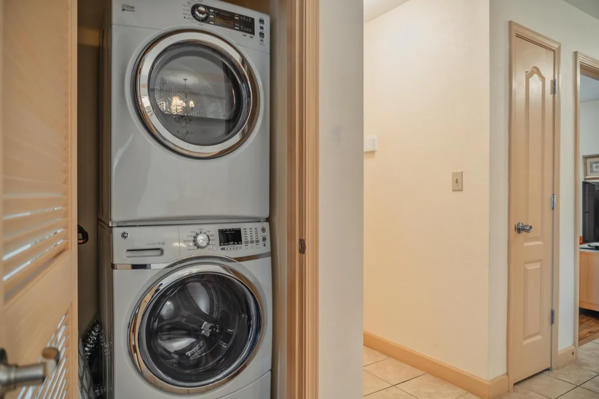 A practical laundry area with a stacked washer and dryer, positioned near a wide doorway that leads to another room. The space is uncluttered and efficiently laid out, suggesting easy access for guests with mobility needs.