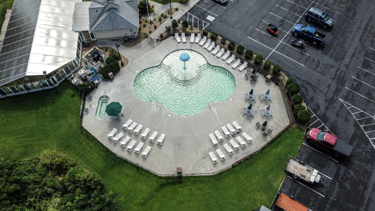 A serene exterior shot of a swimming pool bordered by lounge chairs and lush surrounding greenery. The peaceful atmosphere welcomes both energetic family play and quiet relaxation, suggesting a versatile space for making memories. The natural setting connects with the resort’s spacious five-acre green space.