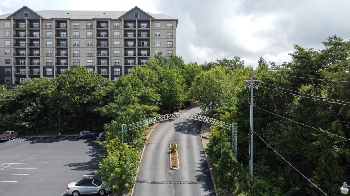 This image captures the entrance archway leading into the property, framed by lush greenery and showcasing the condominium building in the background. The paved road and welcoming landscaping highlight the ease of arrival and the resort’s well-maintained common areas.