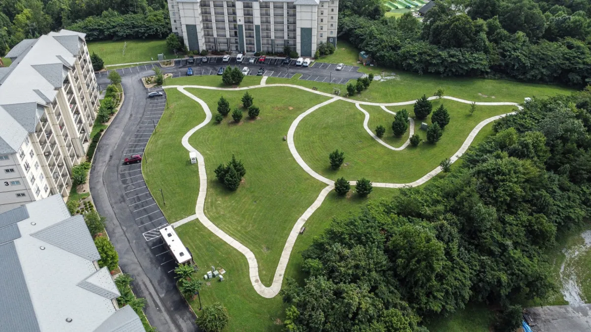 An expansive green space with curved walking paths, scattered trees, and a visible building nearby. The area is well-suited for casual strolls, outdoor gatherings, and connecting with nature on property.