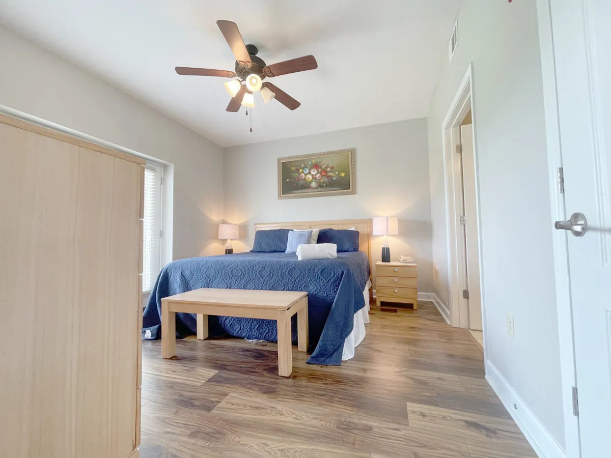 This image showcases a serene bedroom featuring a plush bed adorned with soft linens, a decorative mountain-inspired painting above the headboard, matching nightstands with gentle lighting, and a ceiling fan. The tranquil ambiance invites rest and relaxation, perfect for unwinding after exploring the Tennessee mountains.