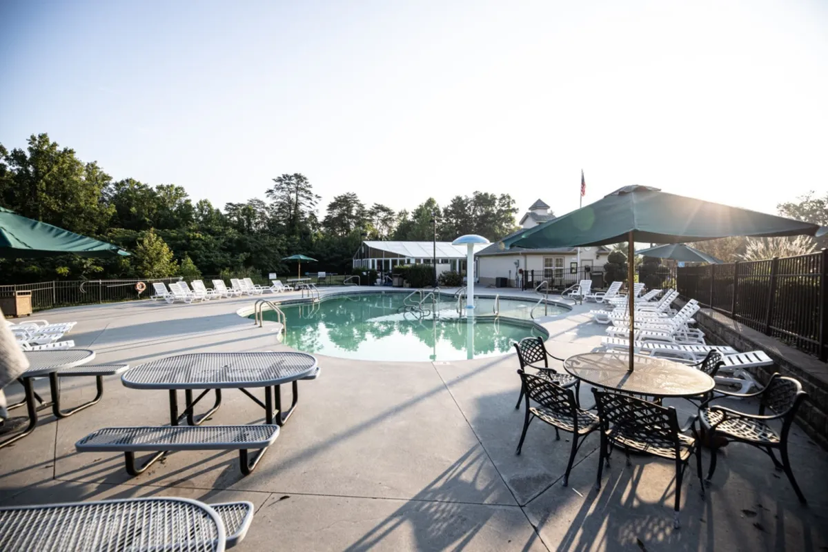 A vibrant exterior view of a resort-style swimming pool surrounded by lounge chairs, tables, and umbrellas. The pool area is inviting and spacious, with ample room for families to gather, play, or relax in the sun. The leisure setting hints at opportunities for poolside barbecues and friendly outdoor gatherings.