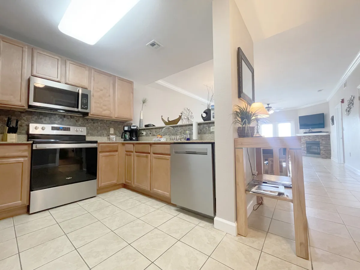 A modern kitchen with stainless steel appliances, granite countertops, wood cabinetry, and an open floor plan that receives natural light from the adjacent living area. The space is ideal for cooking and entertaining.