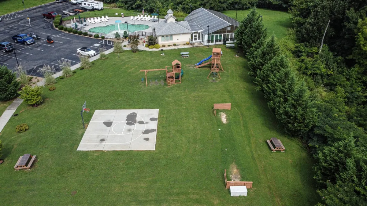 An exterior scene featuring a swimming pool, adjacent basketball court, playground equipment, and picnic tables. The area is bustling with recreational opportunities, set in a lively, communal atmosphere ideal for families and groups.